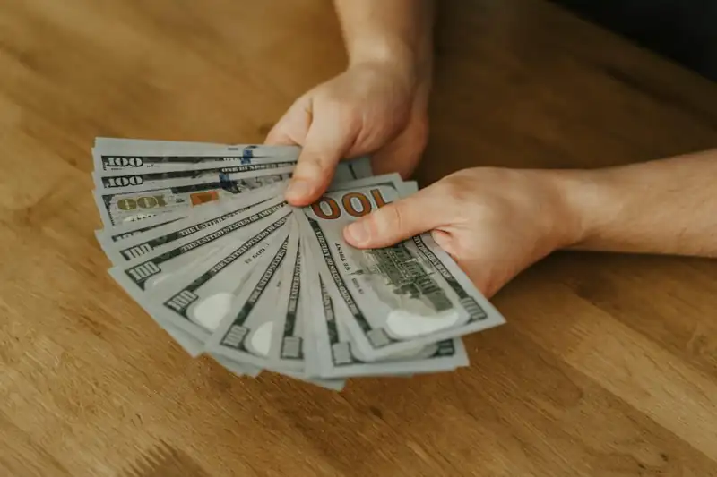 Person holding several $100 bills over a wooden table, representing financial solutions such as Personal Loans Calculator, Personal Loans Near Me, Personal Loans for Poor Credit, Personal Loans Bad Credit, and ways to find Small Personal Loans for everyday financial needs.